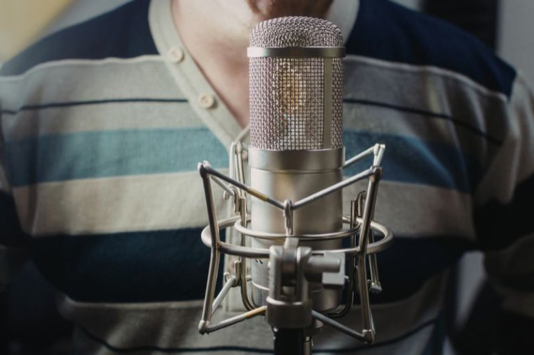Foto mostra em detalhe um homem falando ao microfone