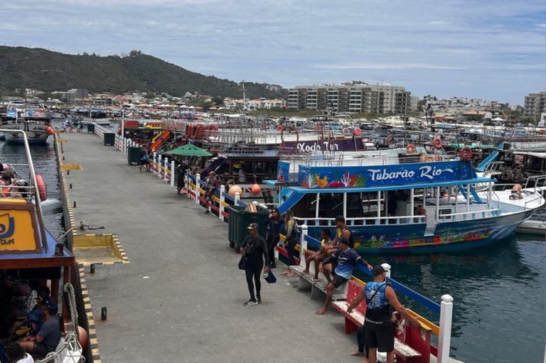 Foto da orla da marina dos pescadores mostra embarcações atracadas e pessoas passando pela calçada