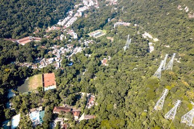 Foto mostra vista aérea de uma área verde, na região do Jardim Botânico, com área verde e linhas de transmissão de energia de um lado, e casas ocupando uma região de outro.