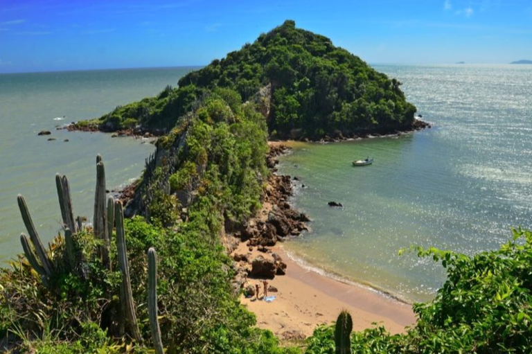 Foto de vista panorâmica do Mirante do Pai Vitório em Búzios, mostrando uma península rochosa e verde que se conecta a uma pequena praia de água clara.