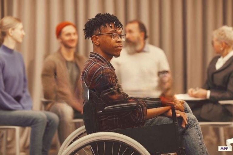 Imagem de um cadeirante negro em uma sala com outras pessoas