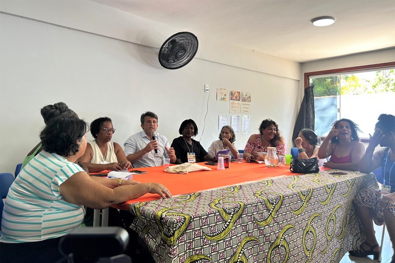 O procurador da República Leandro Mitidieri, representando o MPF, fala ao microfone, ladeado por 9 mulheres, representantes de comunidades tradicionais, todos sentados à mesa do evento da 1ª Conferência Livre do Meio Ambiente de Armação dos Búzios (RJ)