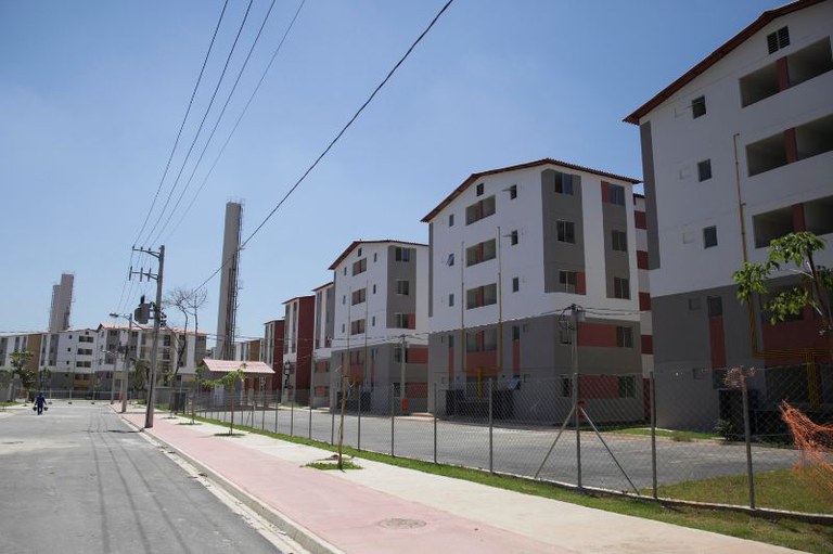 Foto mostra a rua e três prédios de apartamentos