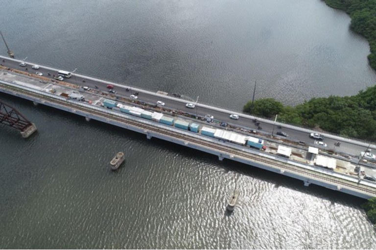 Foto mostra foto aérea da ponte sobre o Rio Pontengi em Natal com águas dos dois lados, vegetação e carros passando por cima