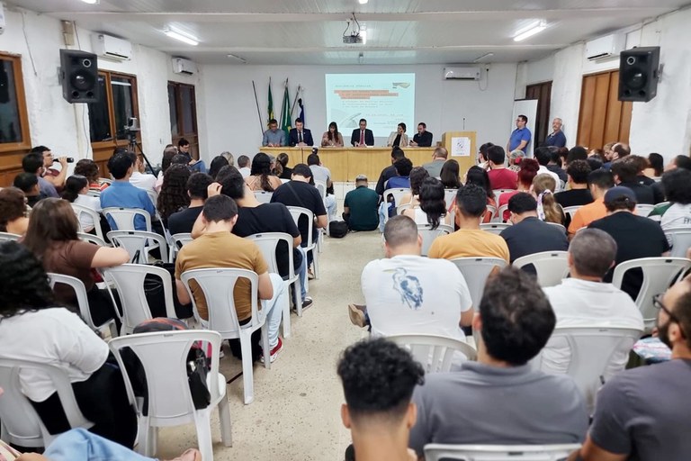 Imagem do fundo do auditório durante a audiência com o público e mesa de participantes à frente.