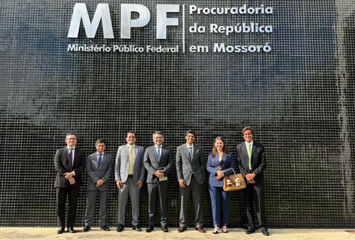 Foto dos participantes da visita e dos procuradores que os receberam, posando em frente à fachada da PRM Mossoró, com o letreiro da procuradoria acima deles