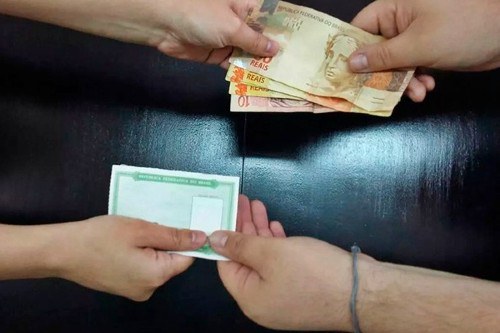 Foto mostra uma pessoa passando o título de eleitor para outra em troca de dinheiro
