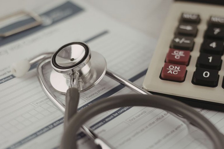 Foto mostra um estetoscópio em cima de um formulário e uma calculadora ao lado
