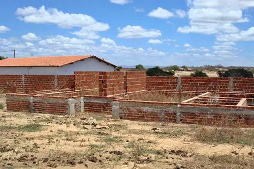 Foto mostra creche com paredes erguidas pela metade e muito mato seco em volta