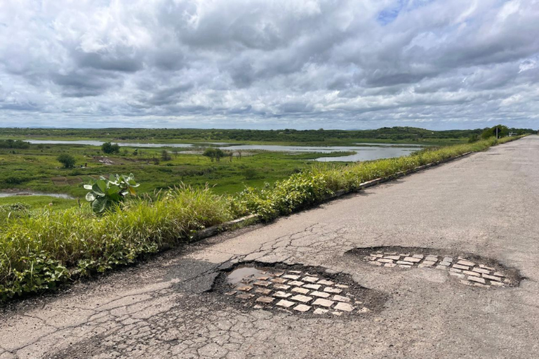 Foto mostra trecho de estrada que passa sobre açude
