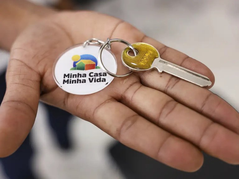 Uma mão aberta segura uma chave com um chaveiro redondo do programa "Minha Casa Minha Vida"