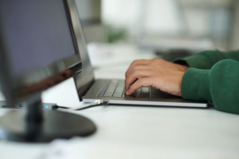 foto em detalhe de uma pessoa com as mãos no teclado de um notebook