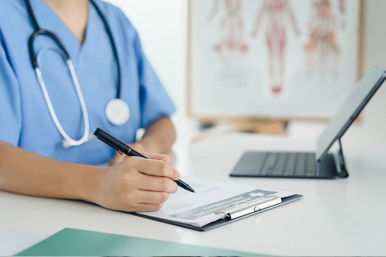 Imagem de uma profissional em hospital preenchendo um papel em uma prancheta
