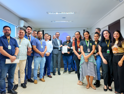 Grupo de pessoas reunidas no auditório do MPF em Porto Velho, posando para fotografia após reunião. Ao centro, uma pessoa segura um documento enquanto os demais estão posicionados ao redor. O ambiente possui projetor ao fundo e iluminação interna.