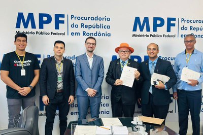 Foto: Comunicação/MPF Foto mostra seis homens com roupas formais em pé lado a lado na frente do banner do MPF