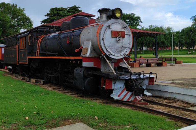 Foto de uma locomotiva a vapor preta e branca (número 18) da Estrada de Ferro Madeira-Mamoré, exposta em um parque.