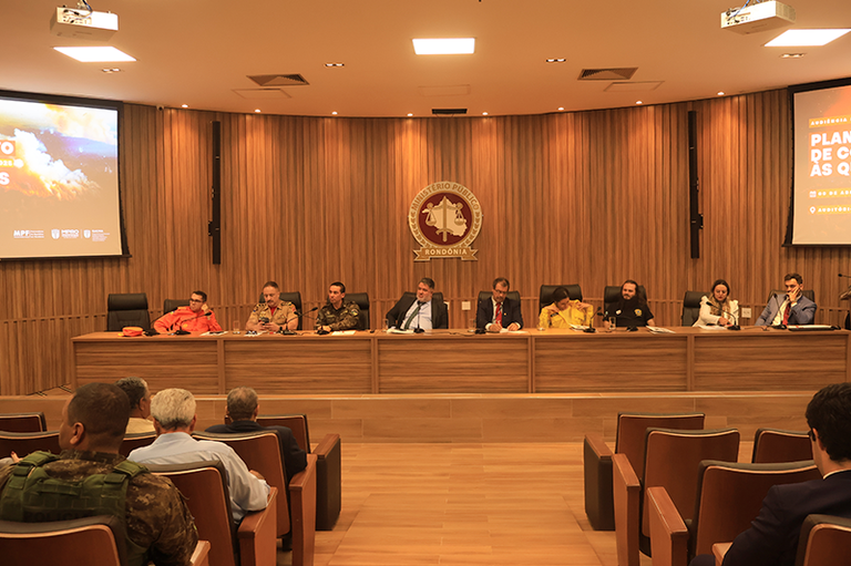 Foto mostra a mesa formada para os debates. Os ouvintes lotam o auditório
