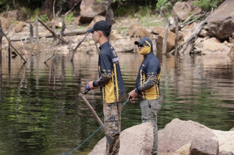Foto mostra dois jovens na beira do rio pescando