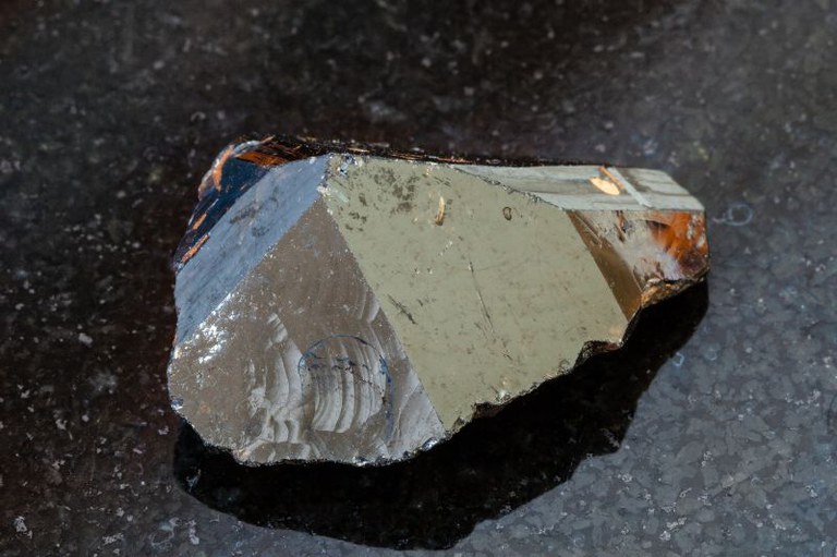 Foto mostra uma pedra de cassiterita na cor cinza escuro