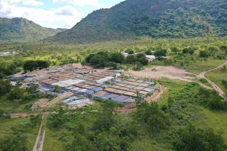Foto aérea de uma área de mineração ilegal com tanques de água retangulares e lamacentos, cercada por vegetação de cerrado e colinas verdes.