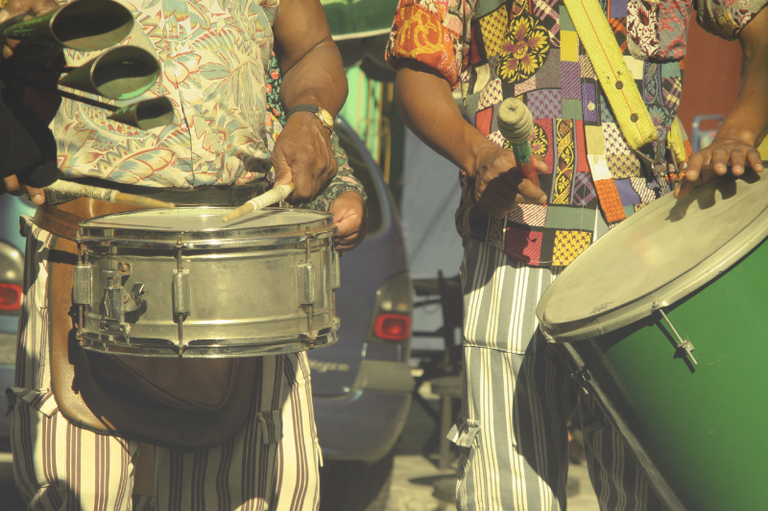 Imagem mostra três ritmistas tocando instrumentos durante desfile de bloco de carnaval