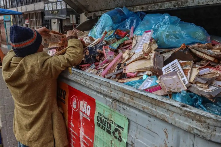 Foto mostra pessoa em situação de rua catando lixo