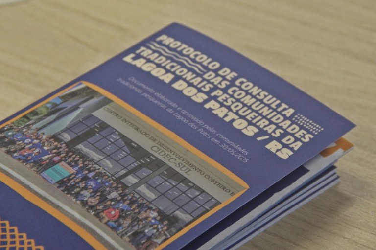 Foto da capa do protocolo de consultas. A foto mostra participantes das comunidades pesqueiras. Em branco está escrito Protocolo de Consulta das Comunidades Tradicionais Pesqueiras da Lagoa dos Patos