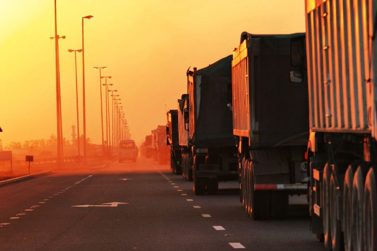 Imagem de uma fila de caminhões uma rodovia ao anoitecer