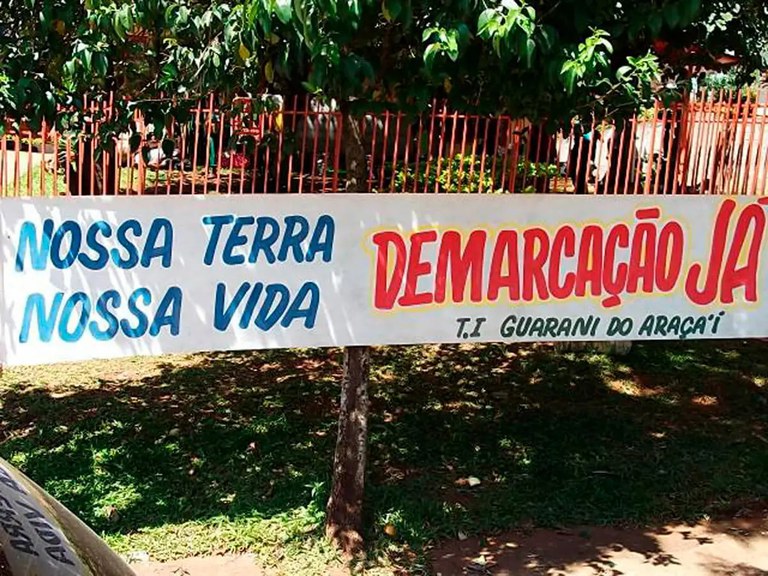 Foto mostra uma faixa pedindo demarcação de terra para os indígenas