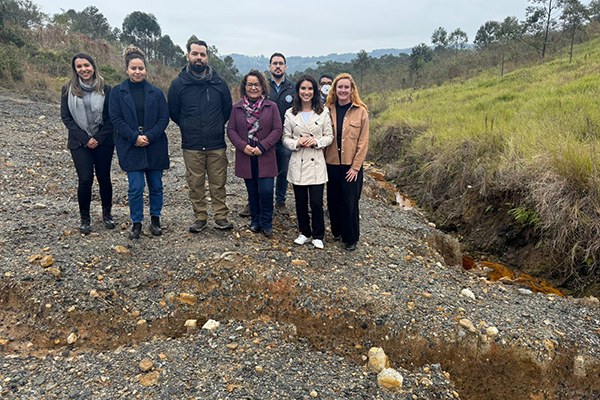 Oito pessoas em pé posam para foto. Elas se encontram sobre um terreno pedregoso. À frente delas, se vê uma rachadura no solo, que se estende de um lado ao outro da imagem