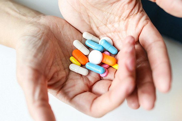 Duas mãos juntas seguram comprimidos de cores variadas.