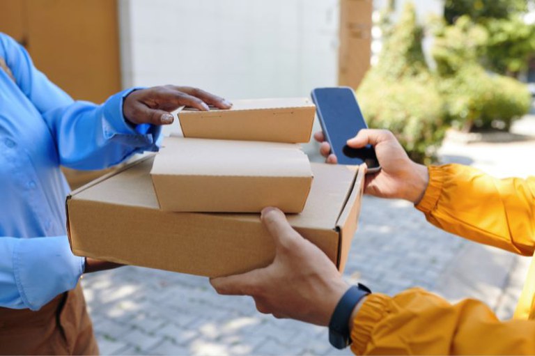 Foto mostra em detalhe uma pessoa recebendo caixas de encomenda em casa