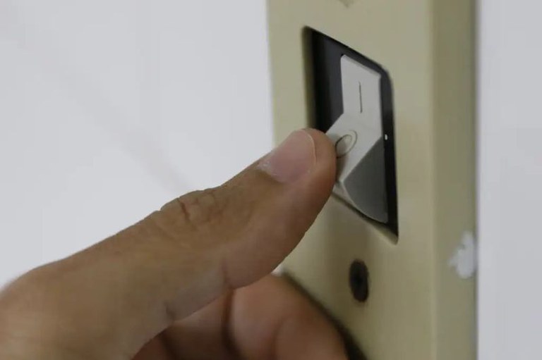 Foto mostra em detalhe uma pessoa apertando um interruptor de energia elétrica