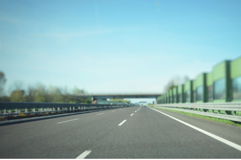 Foto mostra pista de rodovia asfaltada, com barras de proteção nas laterais