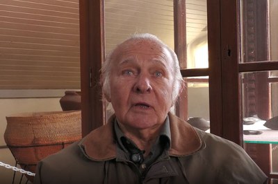 RuiSulzbacher.jpg Homem idoso de cabelos brancos e olhos claros olhando para a frente, vestindo jaqueta marrom. Ao fundo, veem-se grandes vasos cerâmicos e vitrines de madeira de um museu.