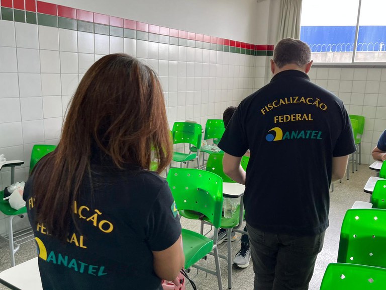 Dois fiscais passando nas salas com aparelho medidor de espectro.