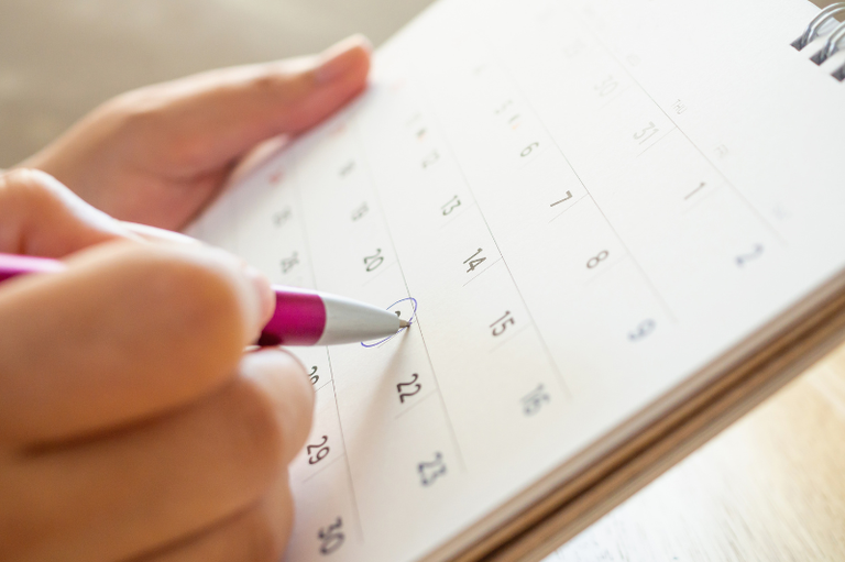 Imagem com uma mão segurando uma caneta e marcando um calendário de mesa
