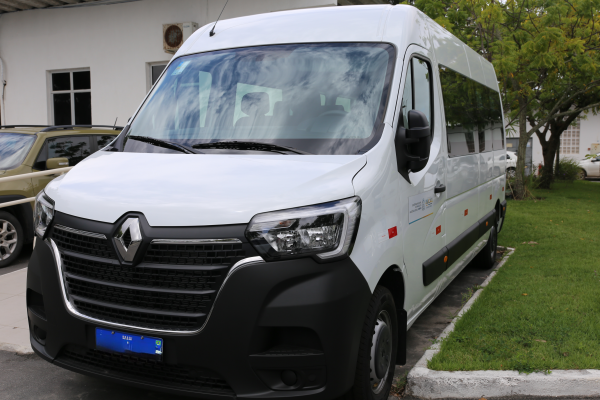 Uma fotografia da parte frontal de uma van branca da marca Renault. A van está estacionada ao lado de uma área gramada, e o nome da cidade de Aracaju pode ser visto no adesivo. O veículo parece novo e limpo, e a placa dianteira é azul, no padrão Mercosul.