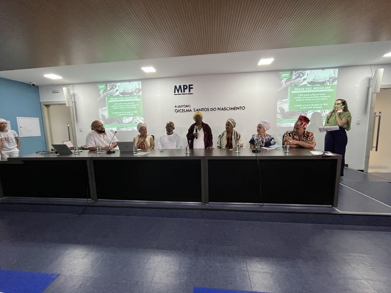 Foto mostra mesa do evento com sete pessoas entre homens e mulheres com microfones e computadores e dois telões atrás com o texto abril verde e a minuta do decreto