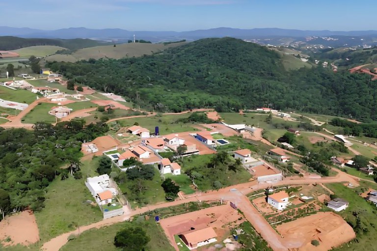 Imagem aérea mostra loteamento residencial, com casas já construídas. Ao fundo, há um morro coberto por mata