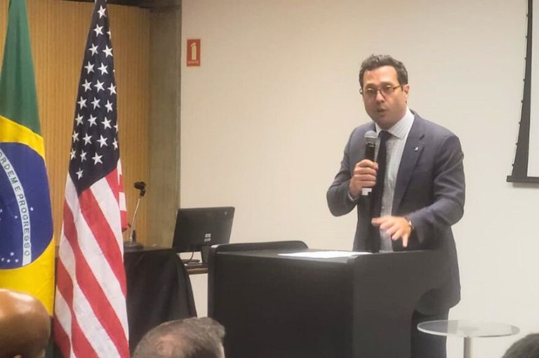 Imagem mostra homem falando em um púlpito ao lado das bandeiras do Brasil e dos Estados Unidos