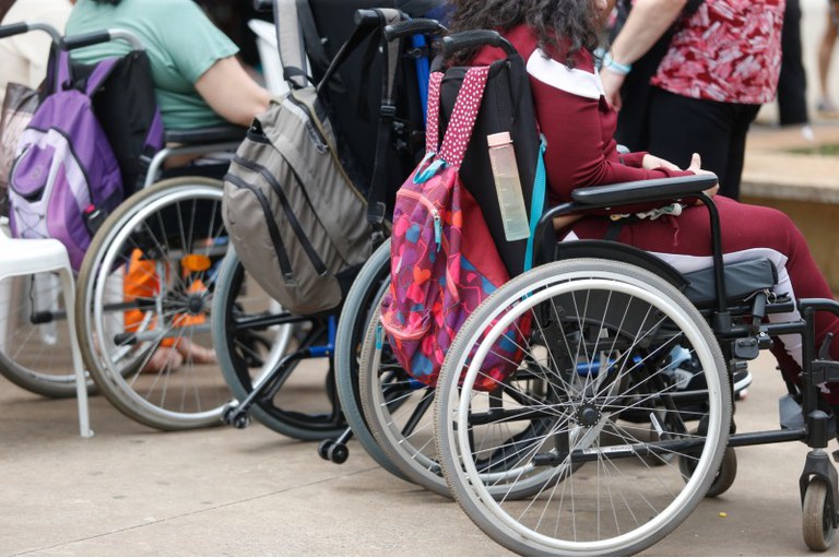 Imagem em detalhe de pessoas em cadeiras de rodas com mochilas penduradas no encosto