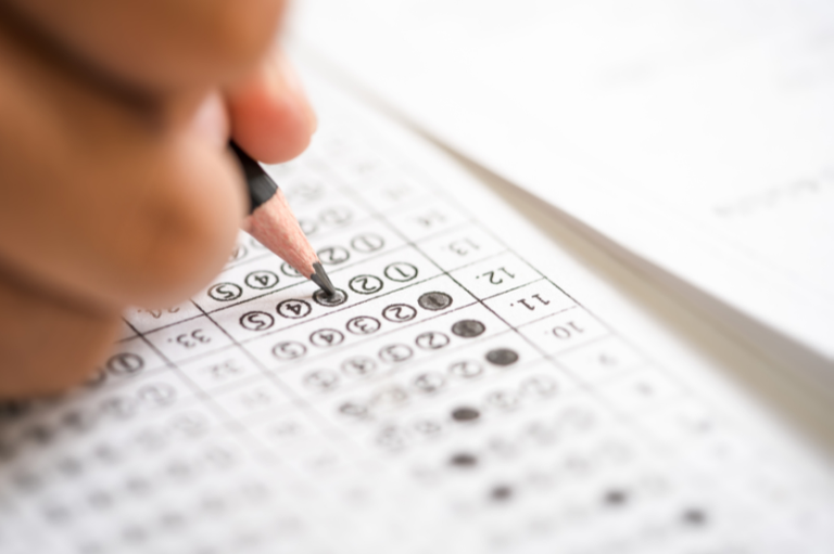 Foto mostra detalhe de uma mão com um lápis sobre folha de prova objetiva de concurso; algumas alternativas da folha estão marcadas