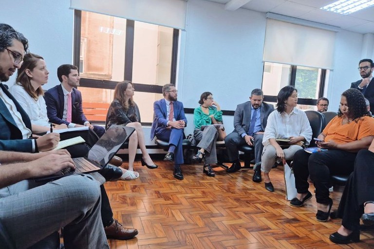 Foto mostra pessoas reunidas em uma sala enquanto um homem fala