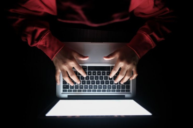 Pessoa encapuzada digitando em um laptop.