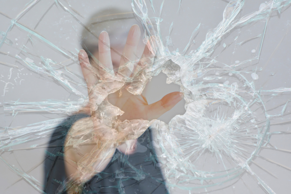 Mulher com a mão estendida em uma atitude defensiva atrás de um vidro quebrado