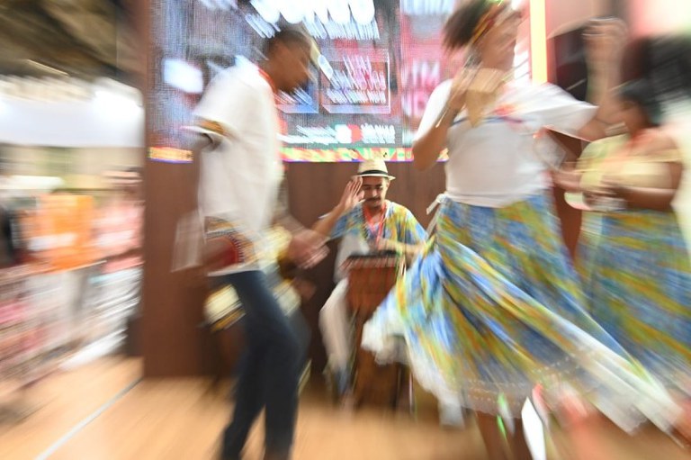 Foto mostra um homem e uma mulher dançando no quilombo. A imagem está um pouco desfocada para dar a sensação de movimento