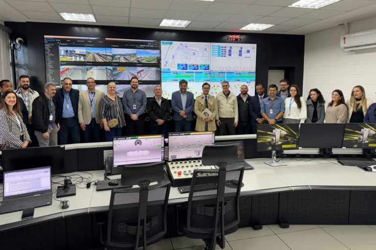 Imagem mostra grupo de pessoas posando para foto na sala do centro de controle operacional do People Mover