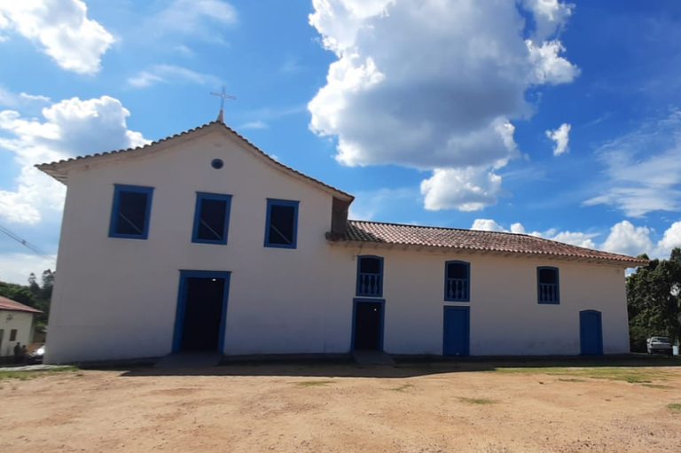 Fachada da igreja, branca com janelas e portas azuis.