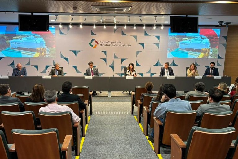 Foto da mesa composta por 6 pessoas. Ao fundo é possível ler Escola Superior do Ministério Público da União. Em primeiro plano é possível ver a plateia.